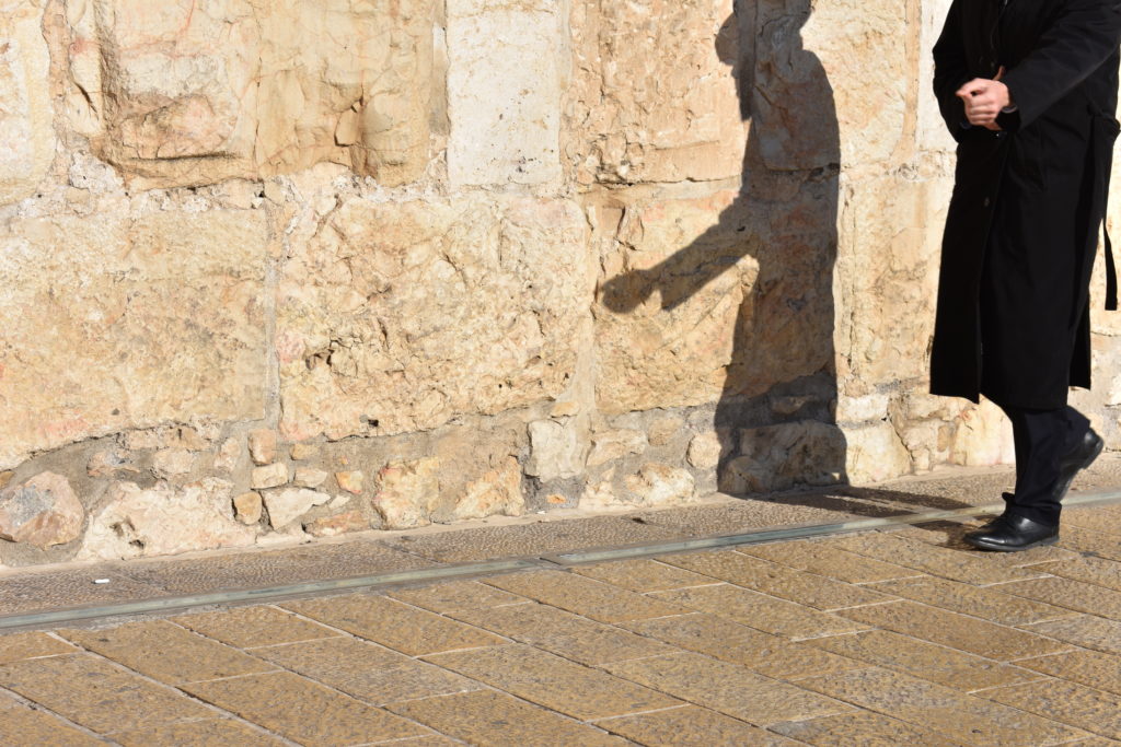 orthodox man walking with his shadow on the wall