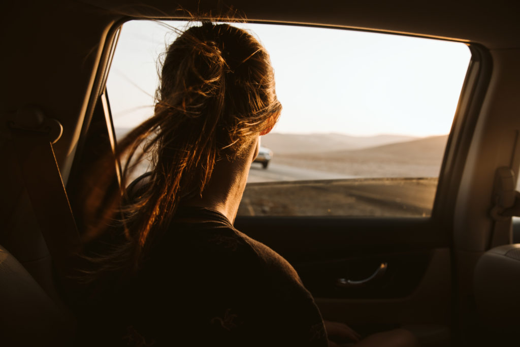 girl looking out the car window at sunset